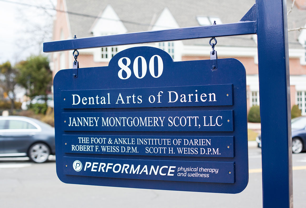 The image features a sign with the name  Dental Arts of Darien  prominently displayed, along with other information such as an address and phone number, set against a backdrop that includes a building and trees.