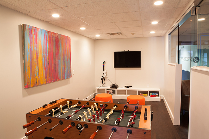 The image shows an indoor recreational room with a pool table, foosball table, and a large painting on the wall.