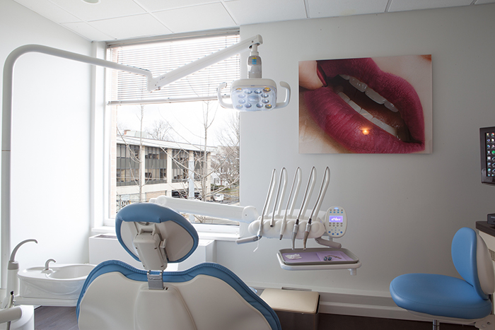 The image shows an interior view of a dental office with dental chairs, equipment, and a large window allowing natural light into the room.