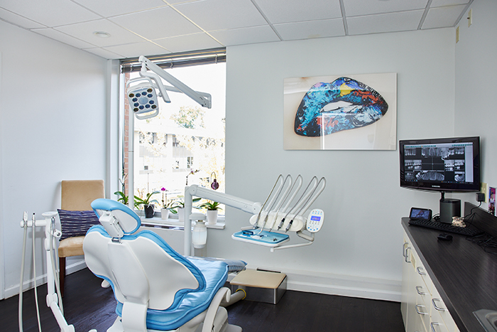 The image is a photograph of an interior space that appears to be a dental office with various pieces of equipment visible, including a dental chair, dental tools, a computer monitor displaying what seems to be X-ray images, and other medical devices.