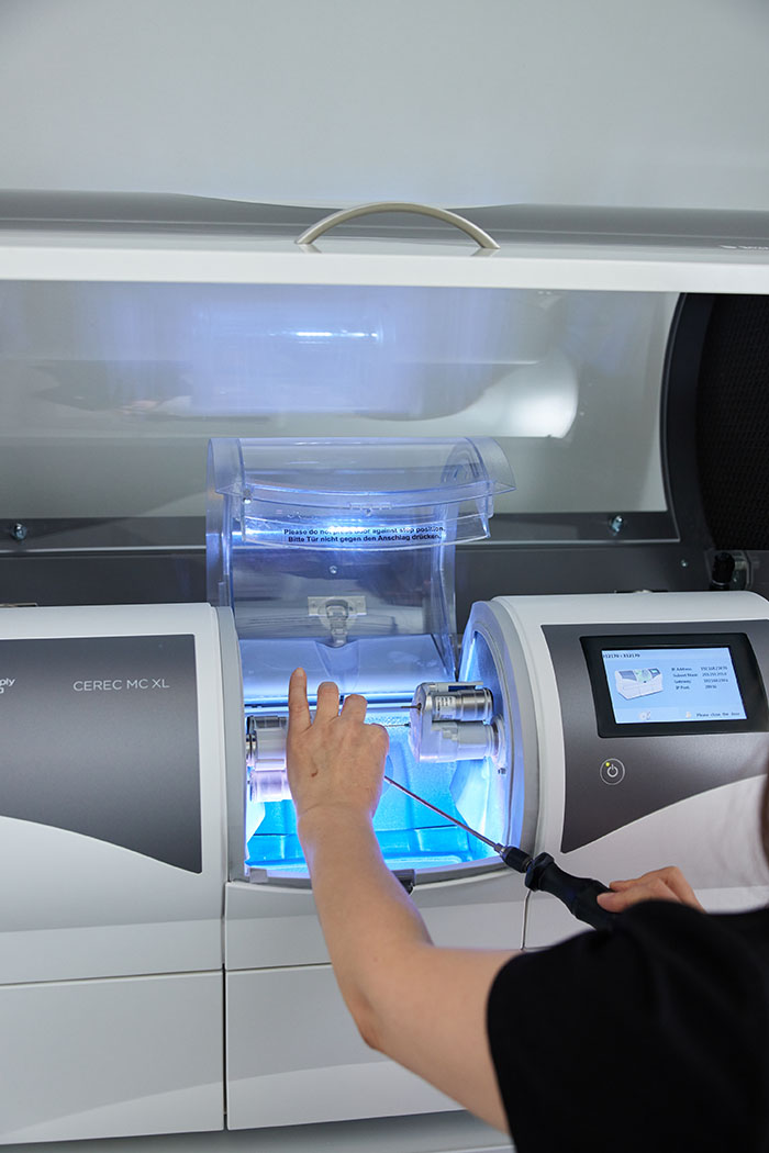 This image shows a person operating a 3D printer with blue liquid inside, indicating that it s in use for manufacturing purposes. The individual appears to be monitoring the printing process closely.
