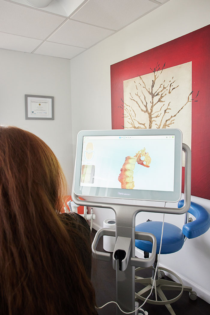 A woman sitting at a dental chair with a digital display showing an animated horse, likely used for patient education or entertainment.