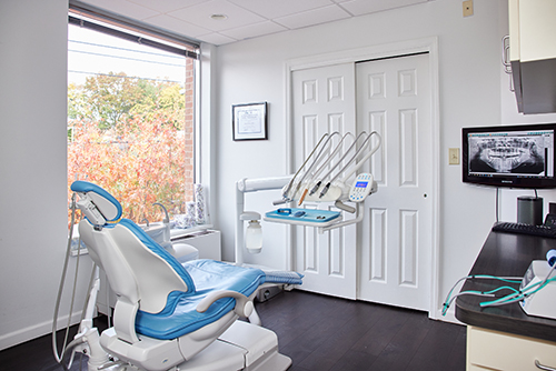 The image shows a dental office interior with a modern dental chair, equipment, and an open door leading to another room.