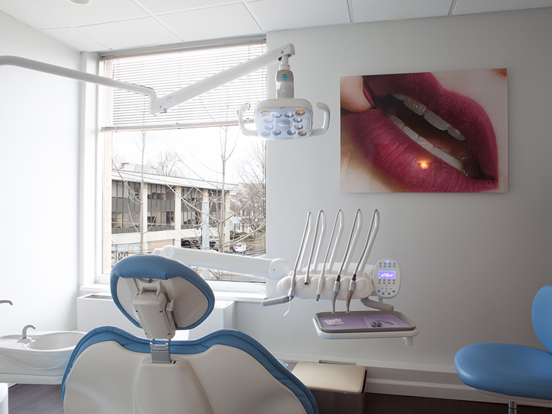 An image of a dental office with a chair, sink, and various dental equipment, including a large mirror and a wall-mounted picture frame.