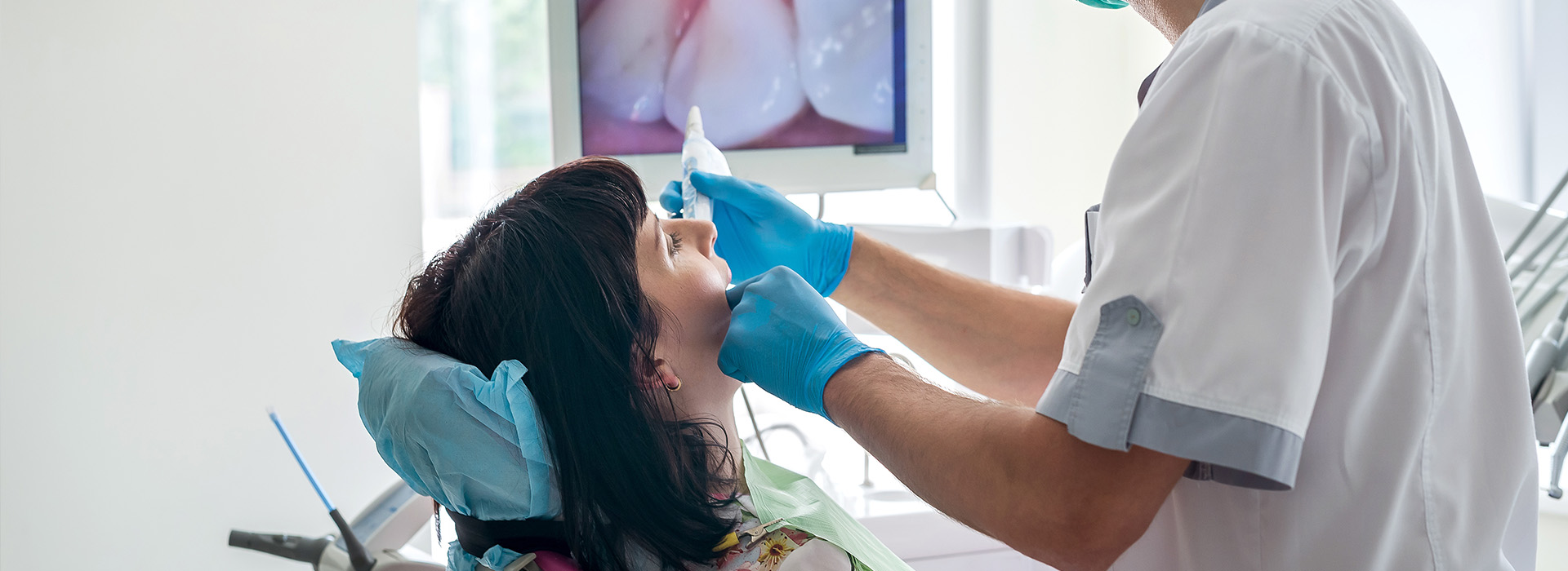 A dental hygienist using a handheld ultrasonic cleaning device on a patient s teeth during a dental procedure.